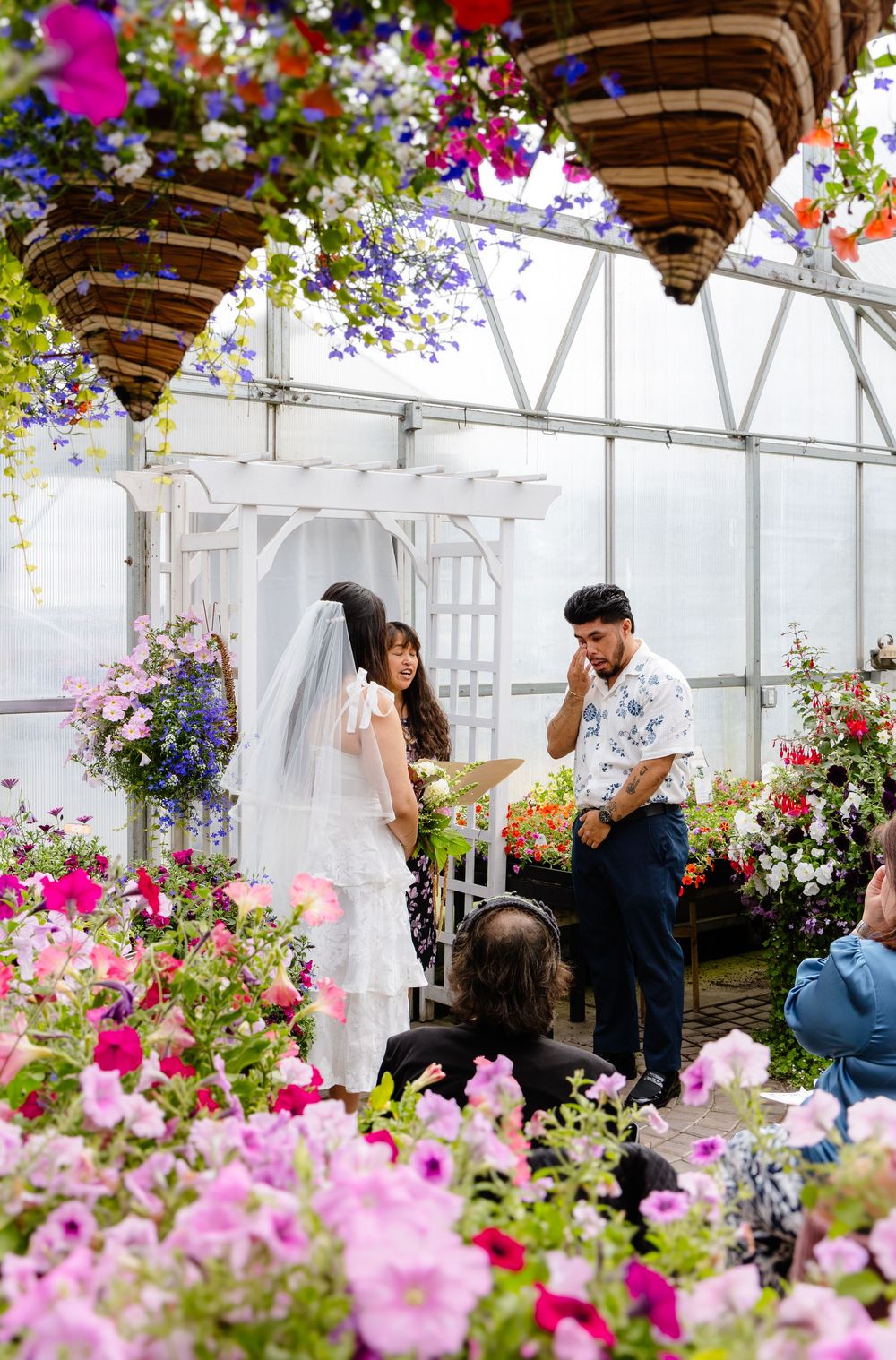People celebrating in a greenhouse setting filled with vibrant pink flowers and hanging decorations.