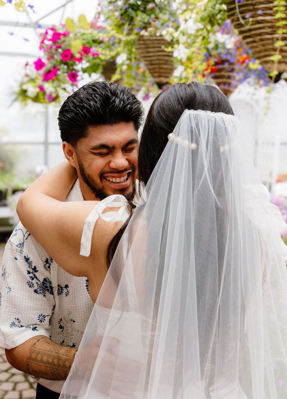 A couple shares joyful laughter and embrace during their wedding photo session in a lush garden setting.