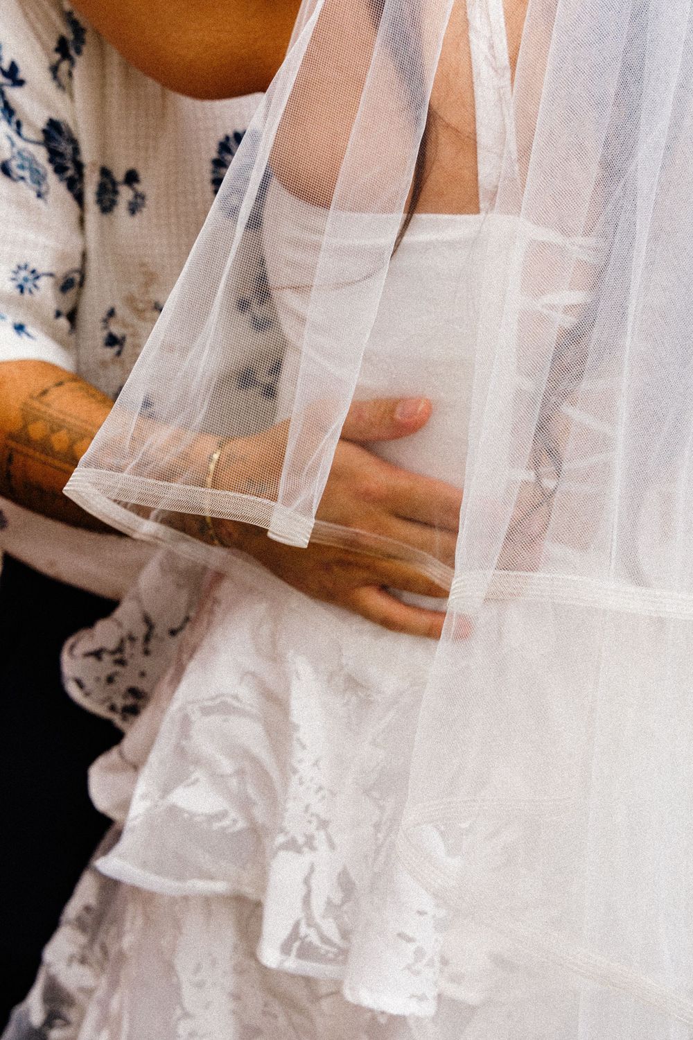 Close-up detail of delicate white tulle and lace on a wedding dress with hands gently touching the fabric.