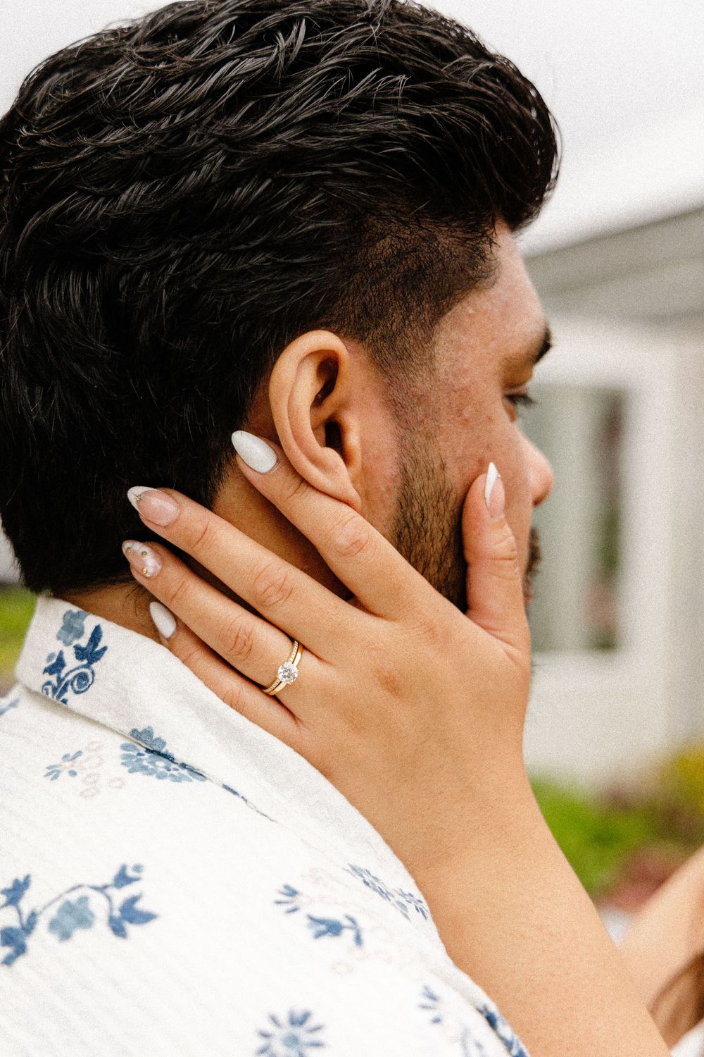 Close up view of a hand wearing a sparkling engagement ring touches someone's neck wearing a floral print shirt.