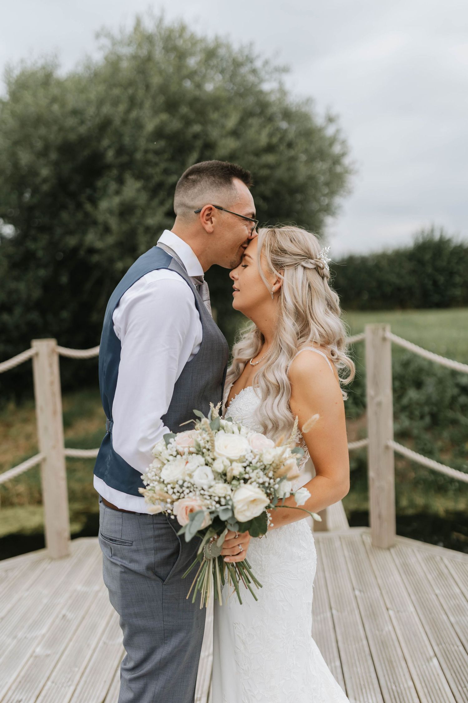 A romantic wedding couple embraces on a wooden boardwalk surrounded by lush greenery on their special day.