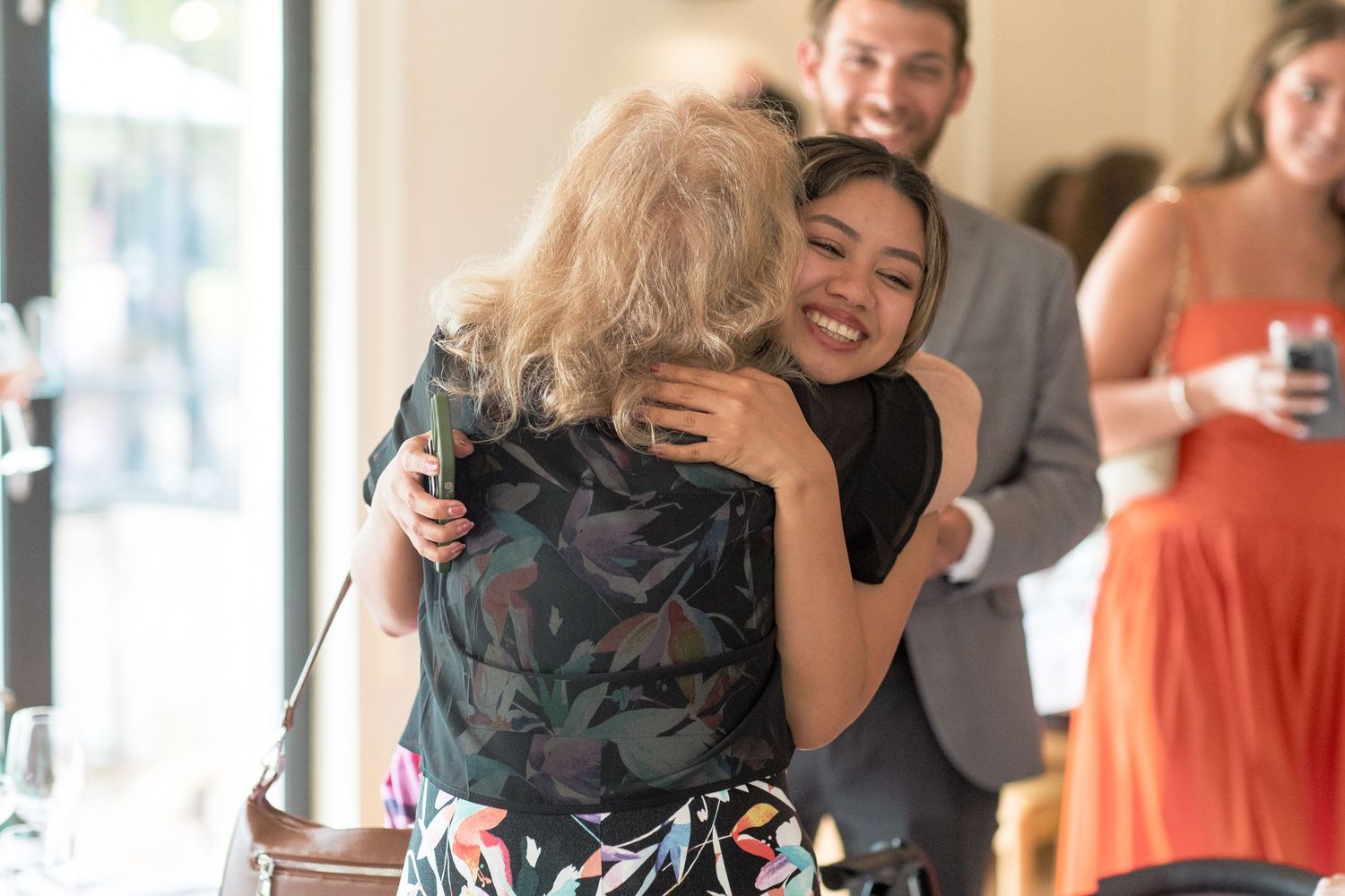 Group of people hugging and embracing in joyful celebration inside a bright indoor space.