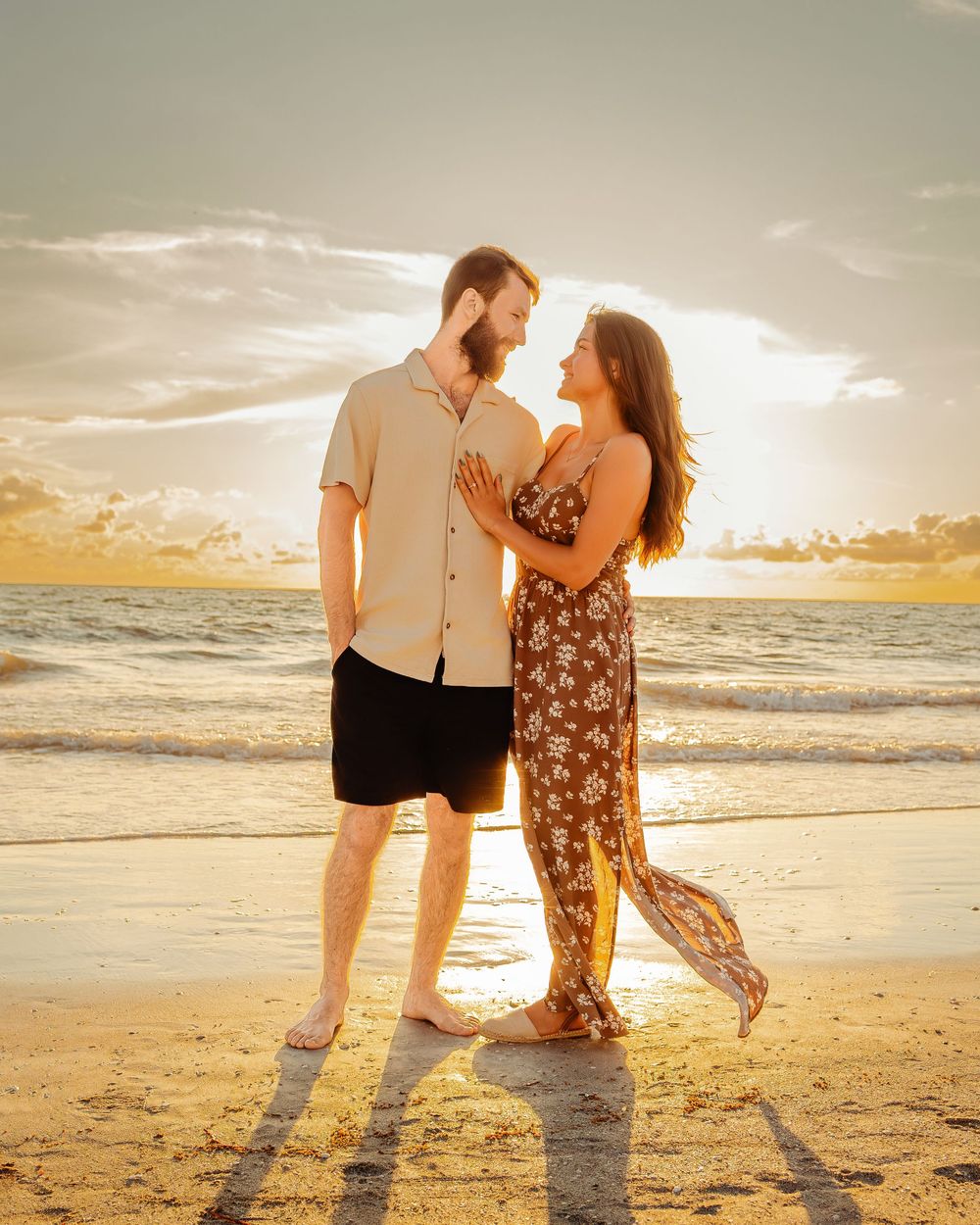 A romantic couple shares an intimate moment on the beach at sunset with golden light illuminating their silhouettes.