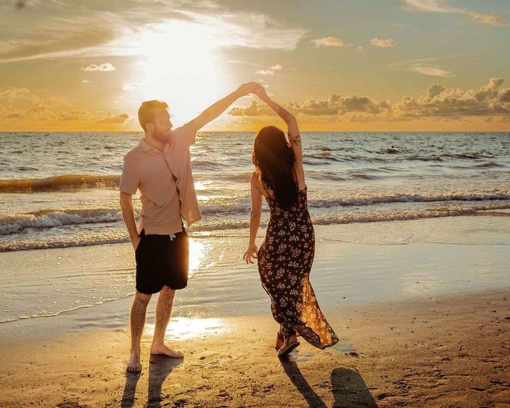 A couple dancing on a beach at sunset with golden sunlight reflecting off the ocean waves.