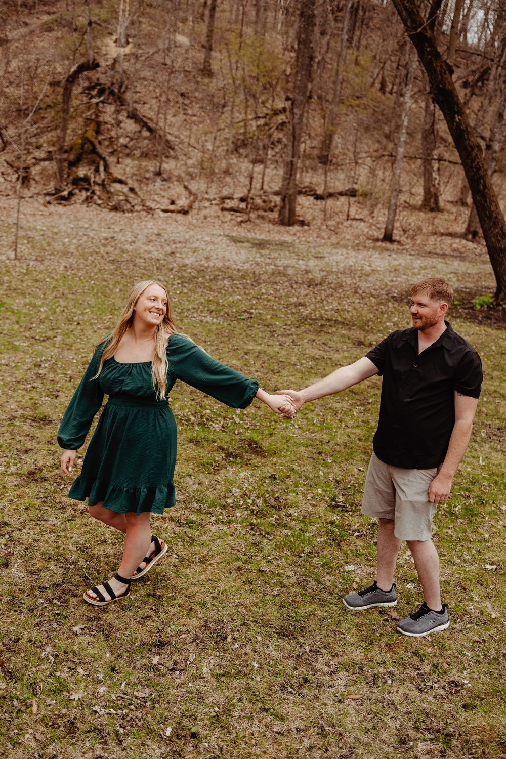 A couple holds hands while enjoying a spring day in the woods, with the person in green twirling playfully.
