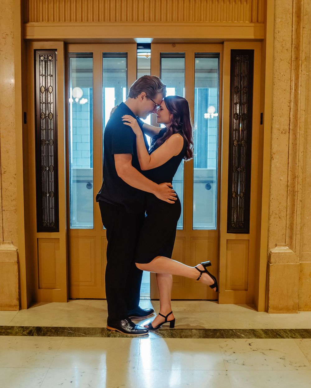 A romantic couple embraces in an elegant hallway with ornate doors and golden walls, creating an intimate moment.