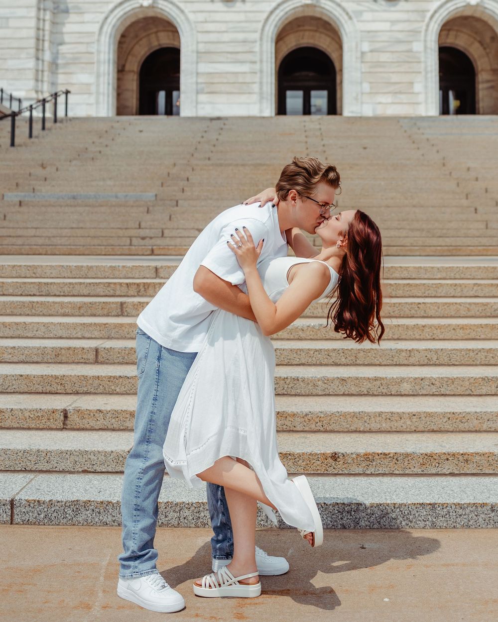 Romantic couple sharing a tender moment on grand stone steps outside an elegant building with arched doorways.
