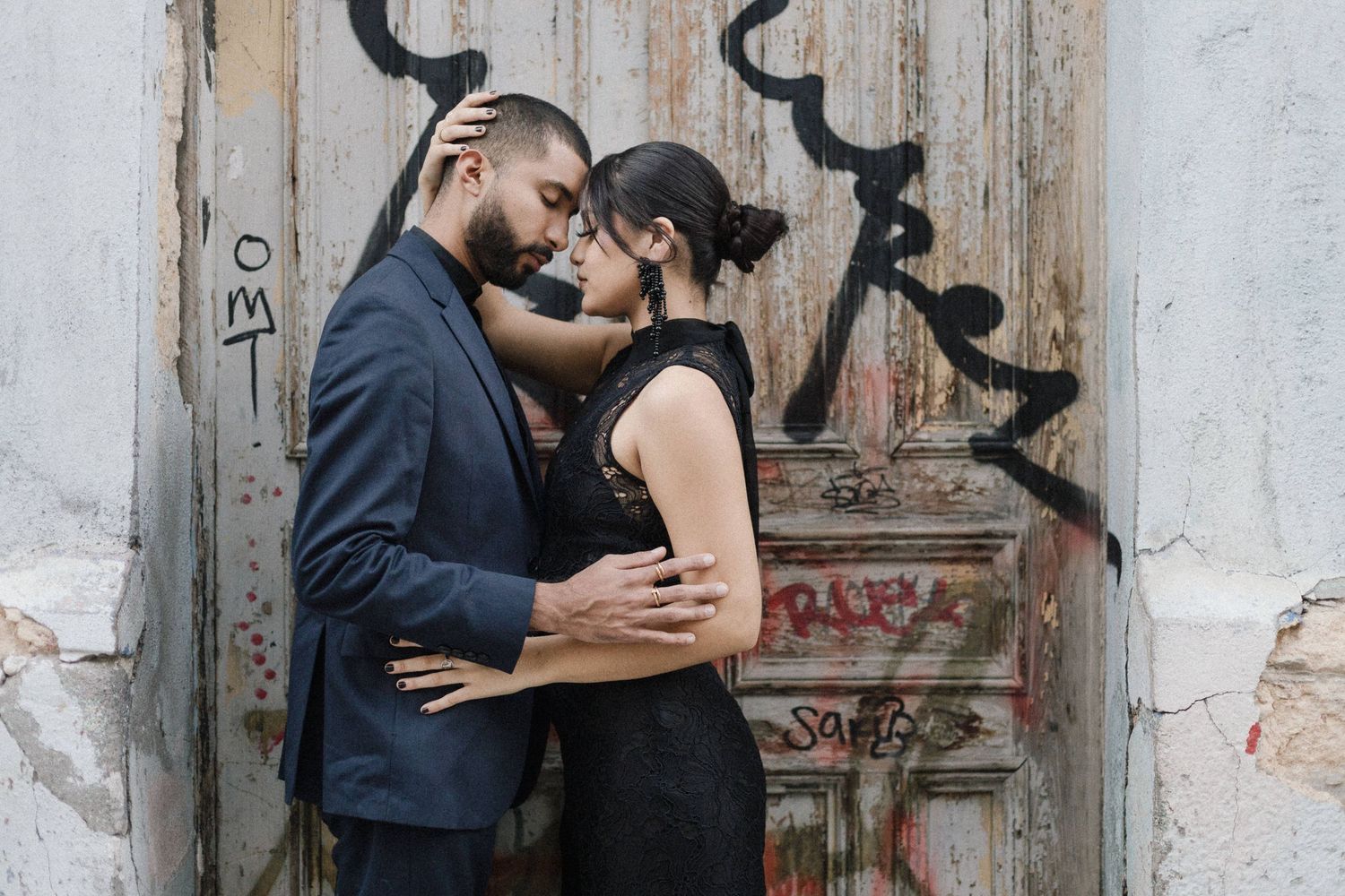 Intimate couple moment against weathered door with graffiti background.