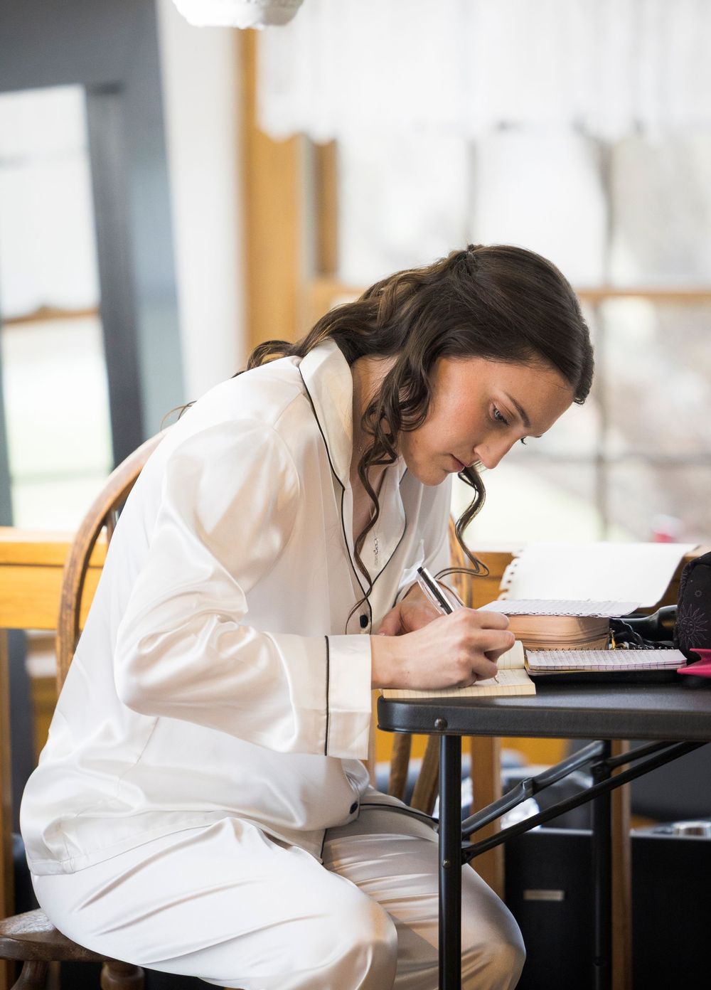 Person in white shirt writing at a desk in a bright indoor setting.