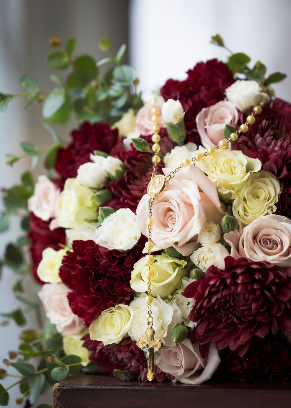 A romantic wedding bouquet featuring burgundy dahlias, blush roses, and cream flowers with eucalyptus accents.