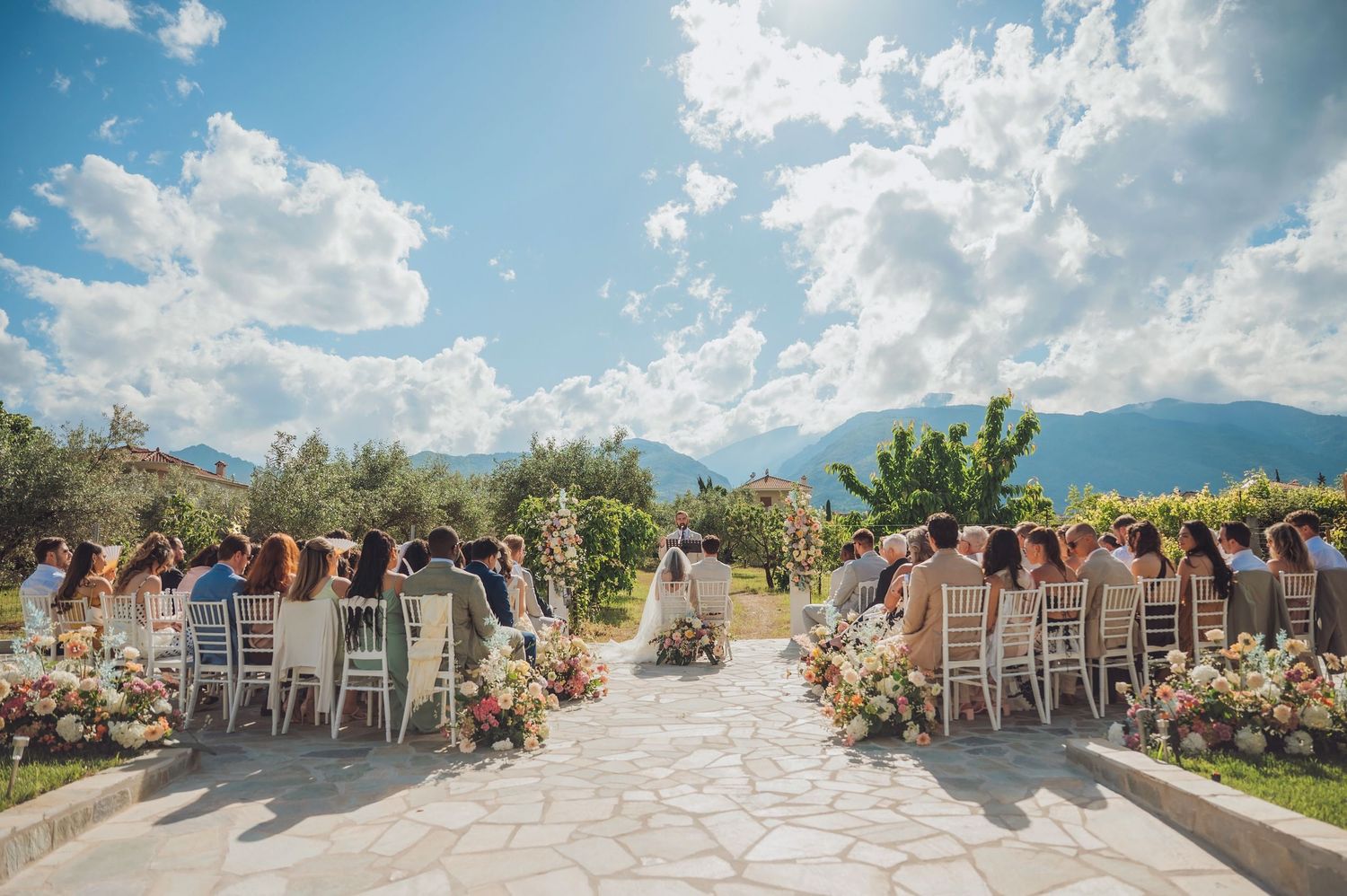 Stunning outdoor wedding ceremony setup with white chairs and floral decorations against a backdrop of mountains and blue sky.