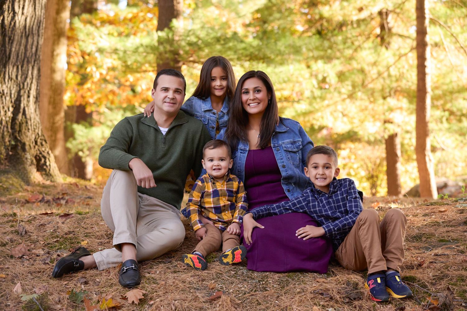 Family relaxing together on colorful fall leaves beneath tall trees in a forest.