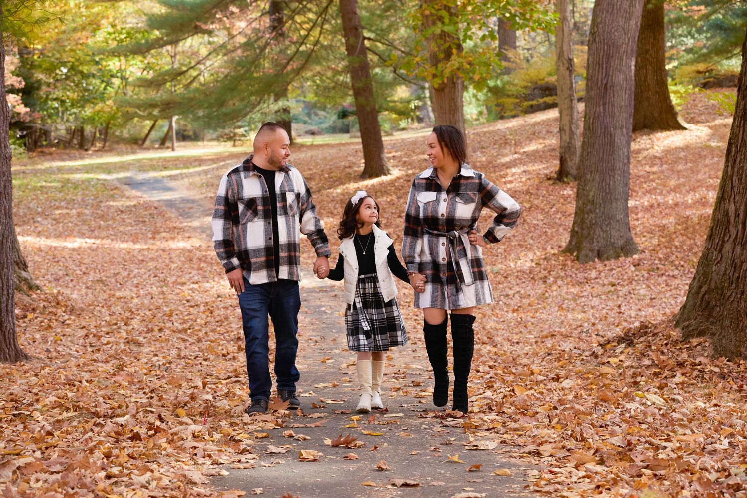 People walking along a leaf-covered path through a forest park with golden autumn foliage and tall trees.