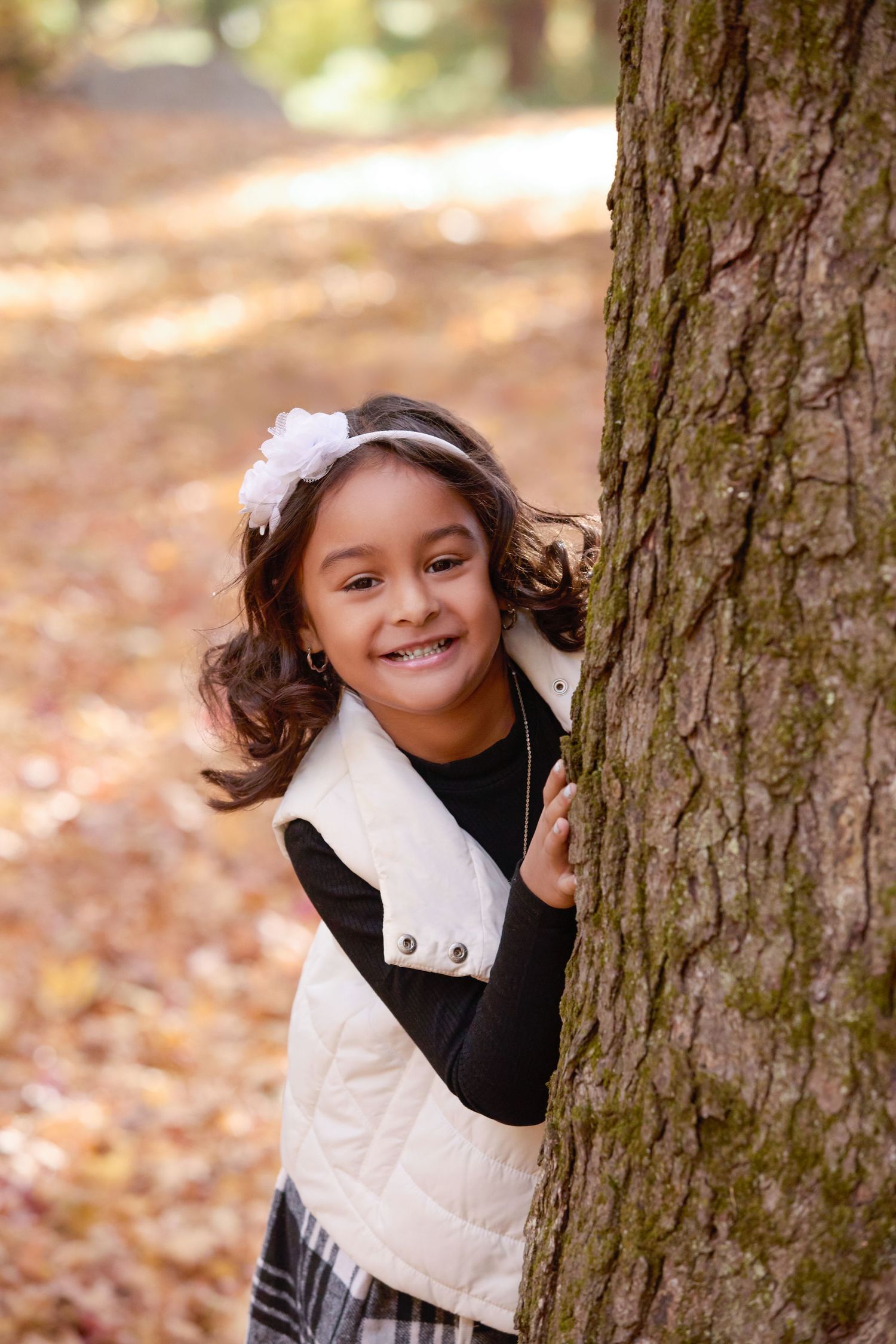 Three photos of a child in a white vest peeking playfully around a tree trunk in autumn.