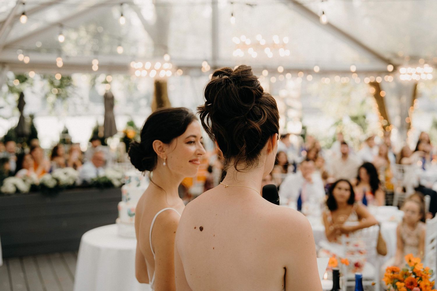 Two brides share a tender moment during their reception in a tent decorated with romantic lighting at the Sanctuary Roosevelt Island