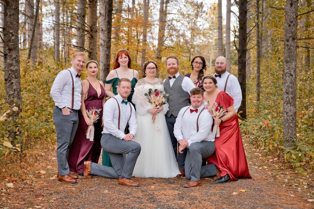 Wedding party celebrates in autumn forest setting with colorful fall foliage and casual attire.