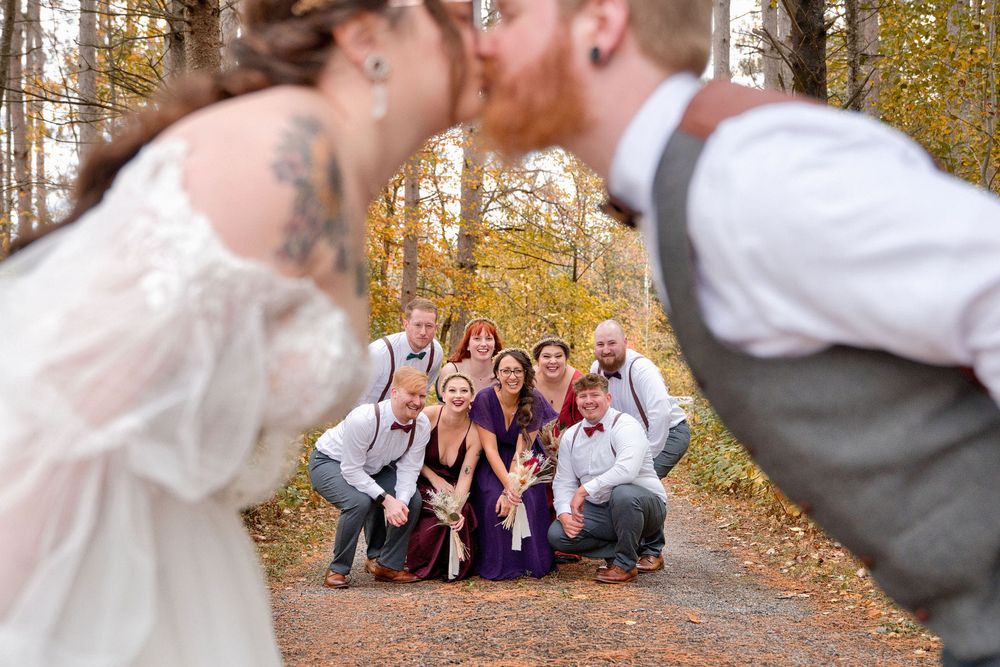 Wedding party members playfully pose in a row on a fall forest path lined with golden autumn trees.