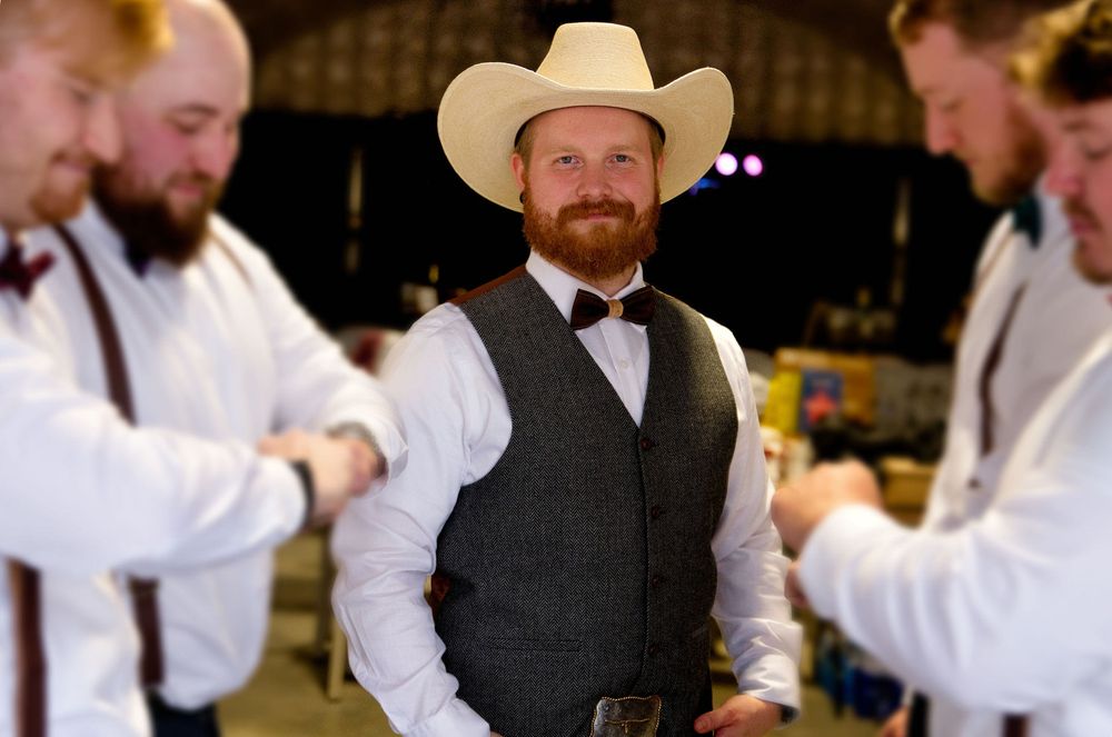 Group of men in formal western attire laugh and celebrate at an indoor wedding reception.