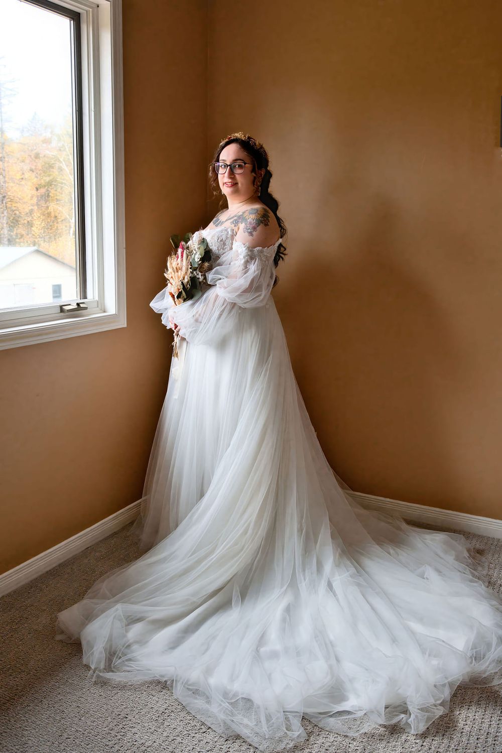 Ethereal wedding dress with flowing tulle train photographed in multiple angles against brown wall and window backdrop.