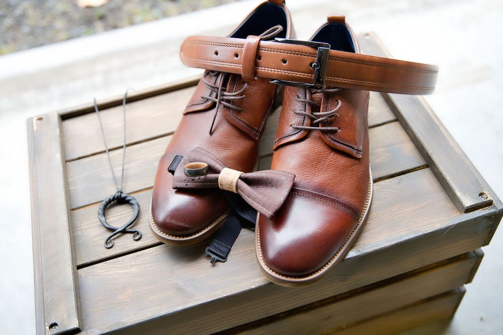 Brown leather dress shoes with a matching belt and pocket watch displayed on a wooden box.
