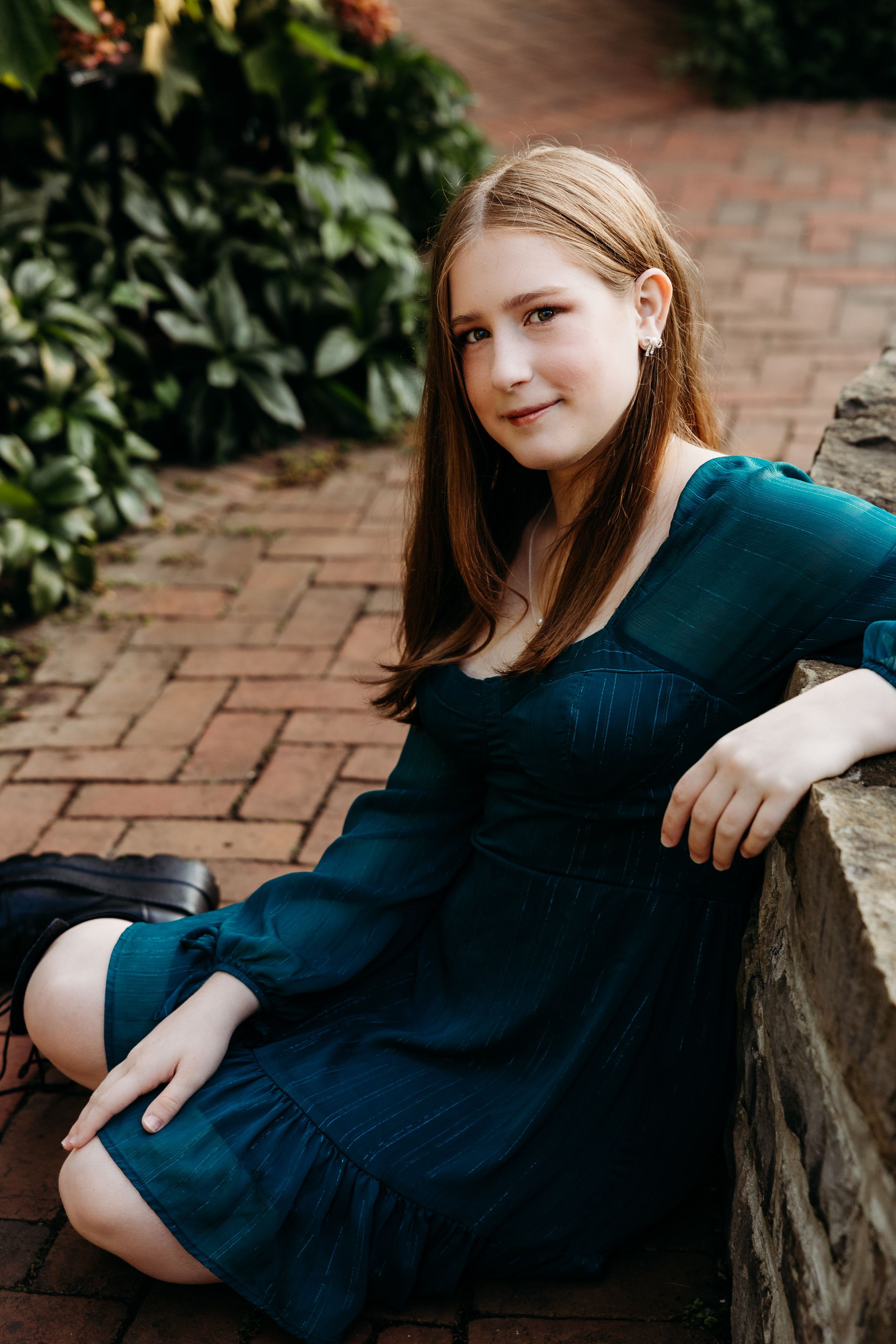 Artistic portrait series on brick patio with dark blue dress and natural garden backdrop.