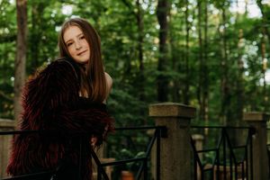 A person with long dark hair poses thoughtfully in a lush green forest setting during a professional photoshoot.