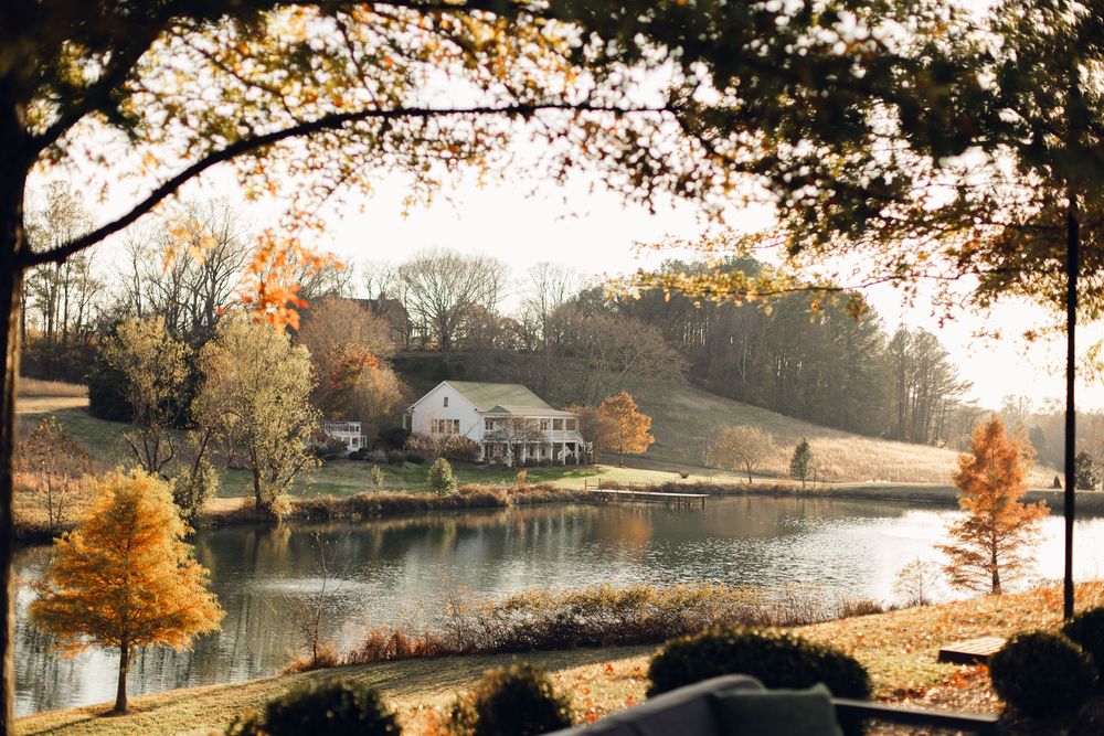 Autumn landscape with a lake reflecting fall foliage and a house nestled on a hillside.