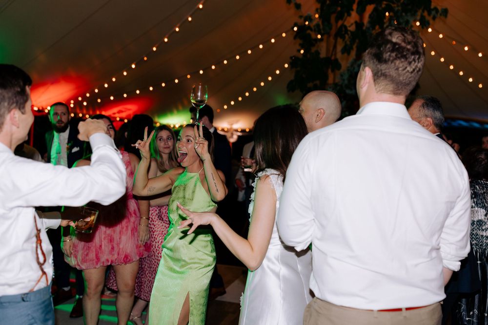 Wedding reception dance party under a tent with string lights and guests dancing.