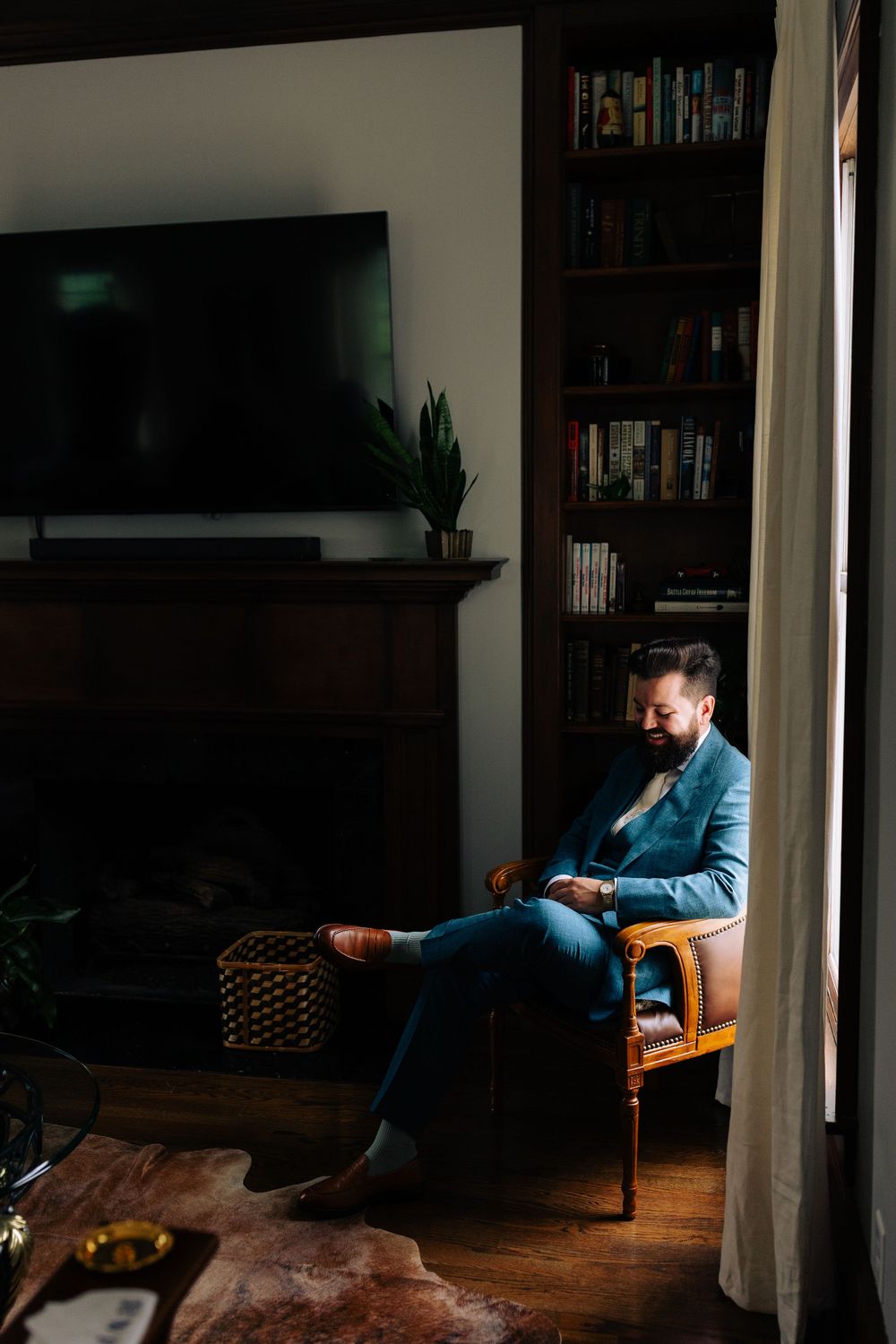 A person in blue attire sits thoughtfully in a room with bookshelves and natural lighting.
