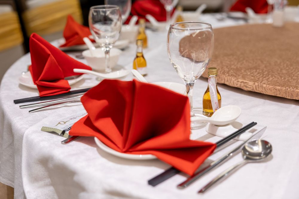 An elegant table setting with bright red napkins, wine glasses, and silverware on a crisp white tablecloth.