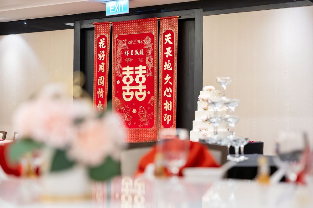 Traditional Chinese double happiness symbol banner and wedding decor with blurred table settings in the foreground.