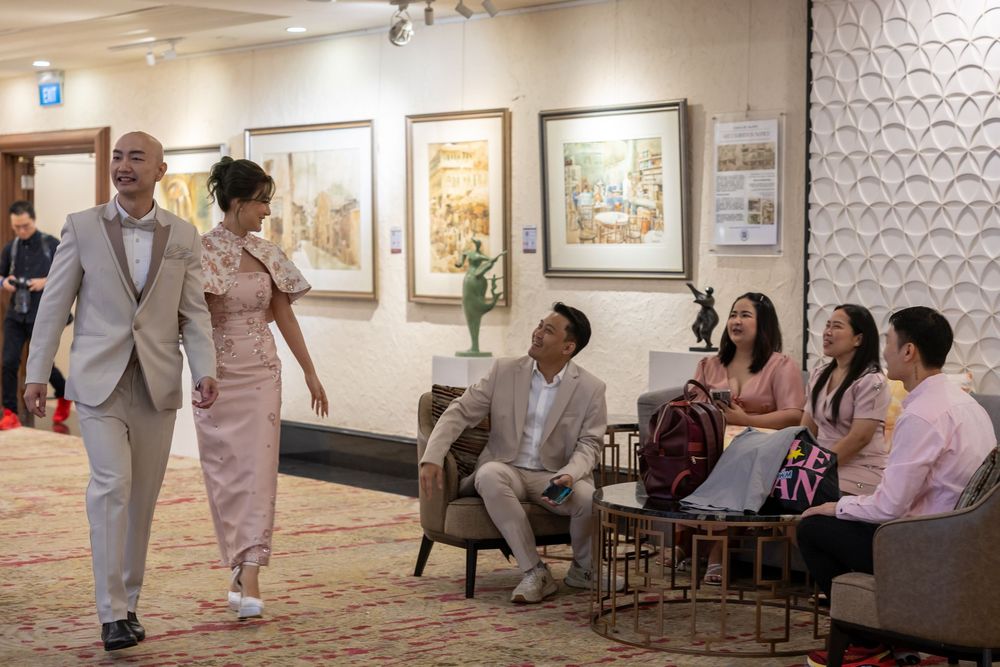 A group of stylishly dressed people gathered in an art gallery hallway with framed artwork displayed on the walls.