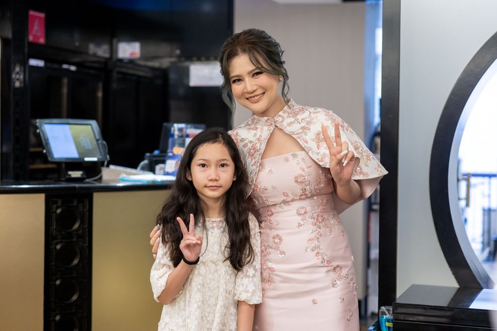 Two people wearing pink dresses pose together in an office setting, showing peace signs and warm smiles.