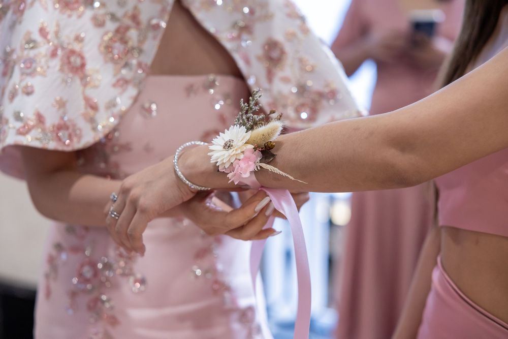 A delicate pink and white corsage with baby's breath being placed on someone's wrist at a formal event.