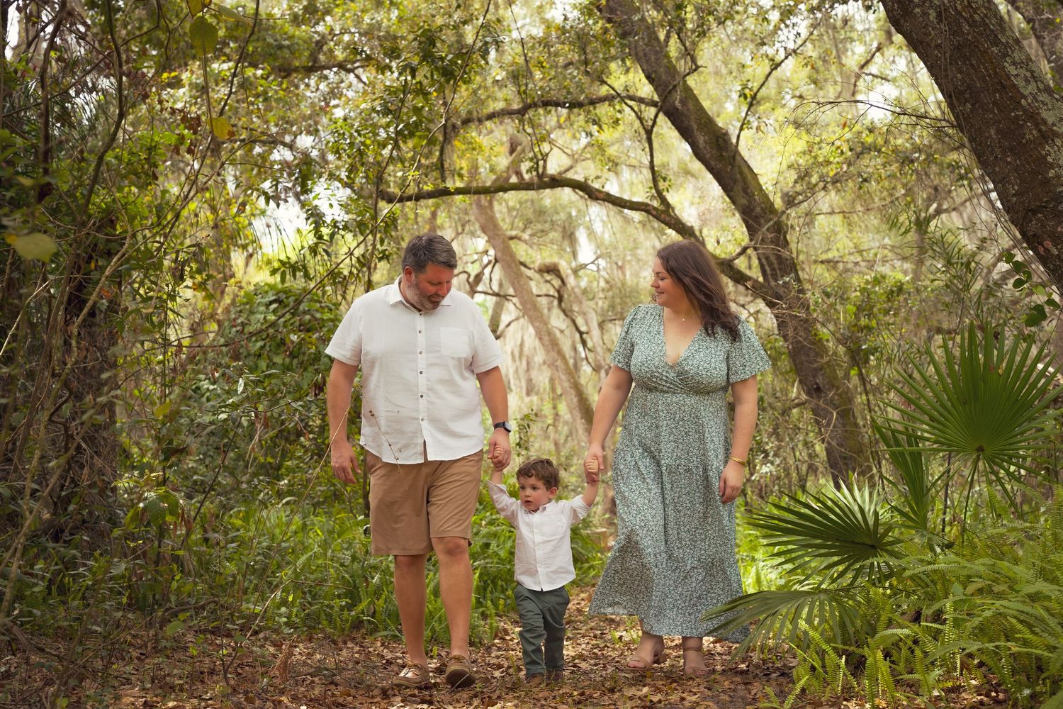 Family walking together through lush green foliage and palm trees on a nature trail.