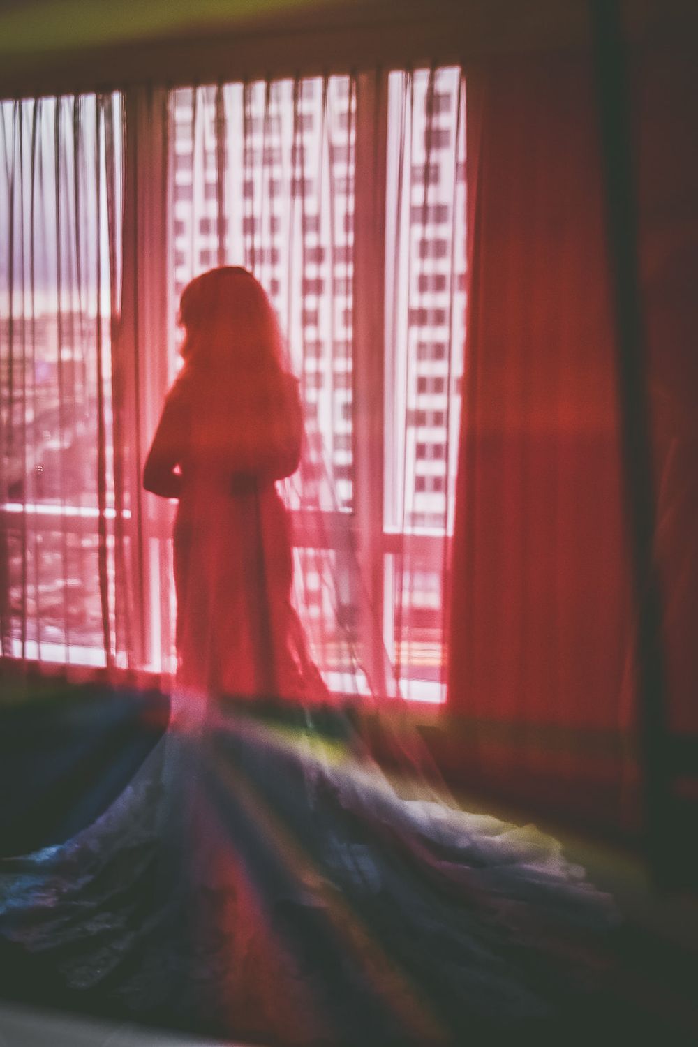 Moody silhouette against a pink-tinted window with gingham curtains creates a dreamy atmospheric scene.