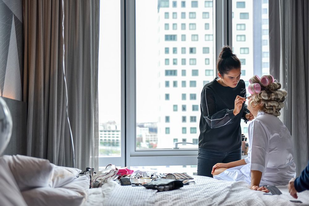Professional hairstylist styling a client's hair while working in a modern hotel room with city views.