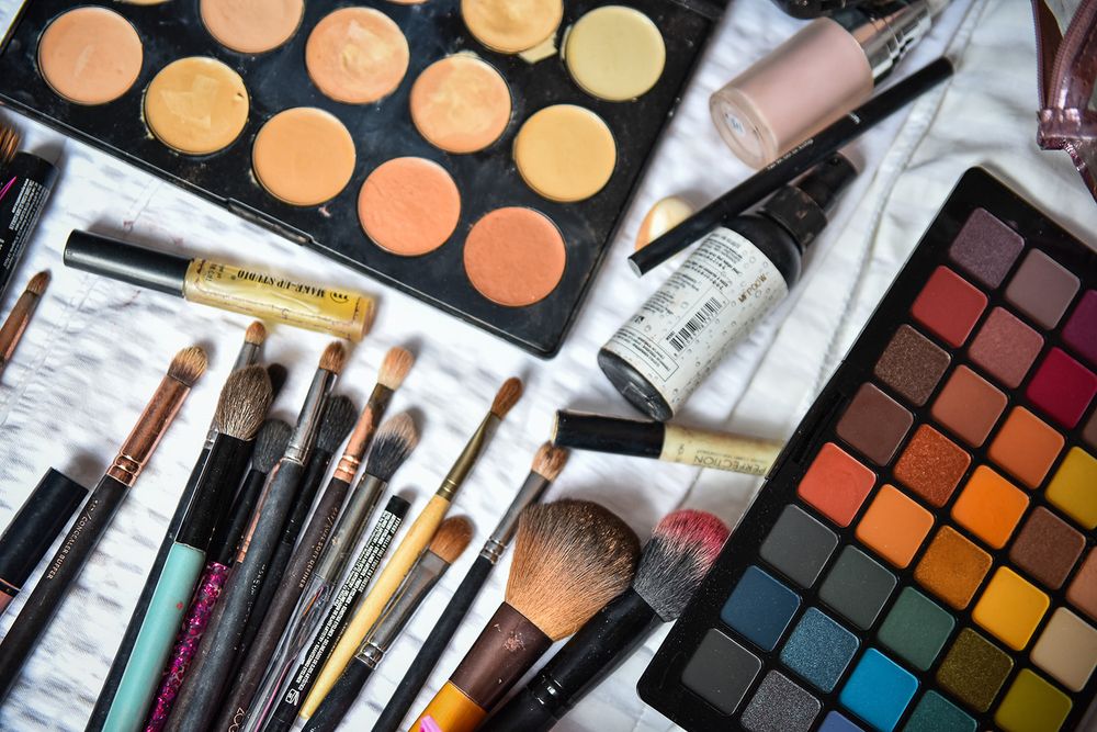 Professional makeup tools and palettes including colorful eyeshadows, foundation shades, and makeup brushes arranged on light surface.