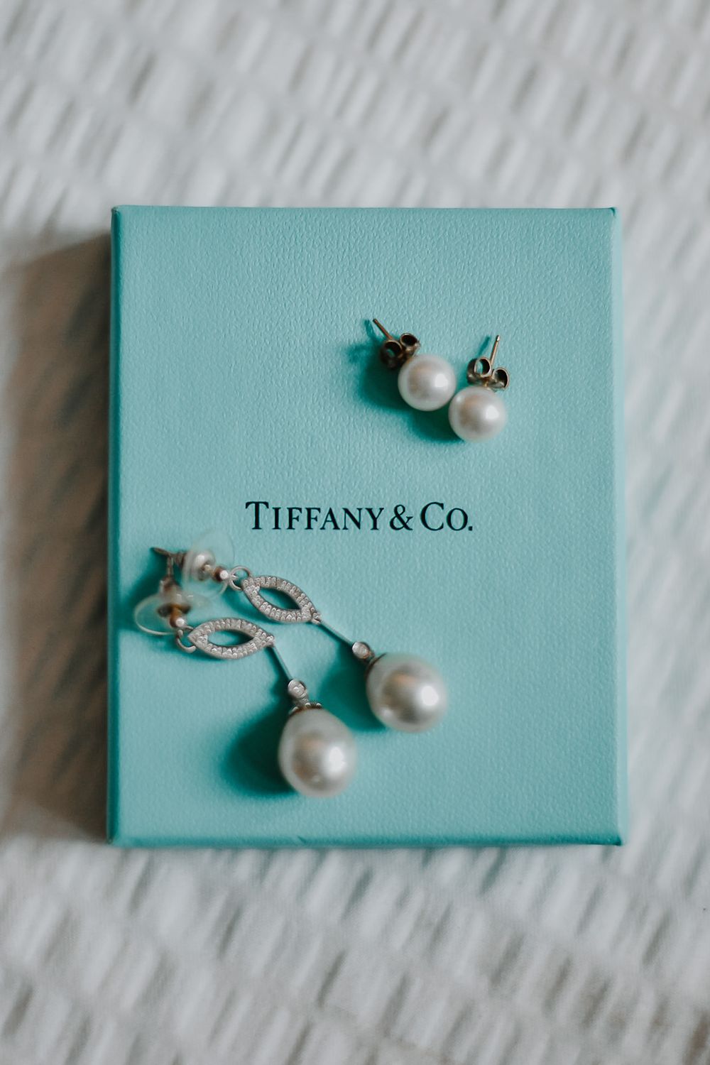 Pearl and diamond Tiffany & Co. stud earrings displayed on iconic light blue boxes in multiple angles.