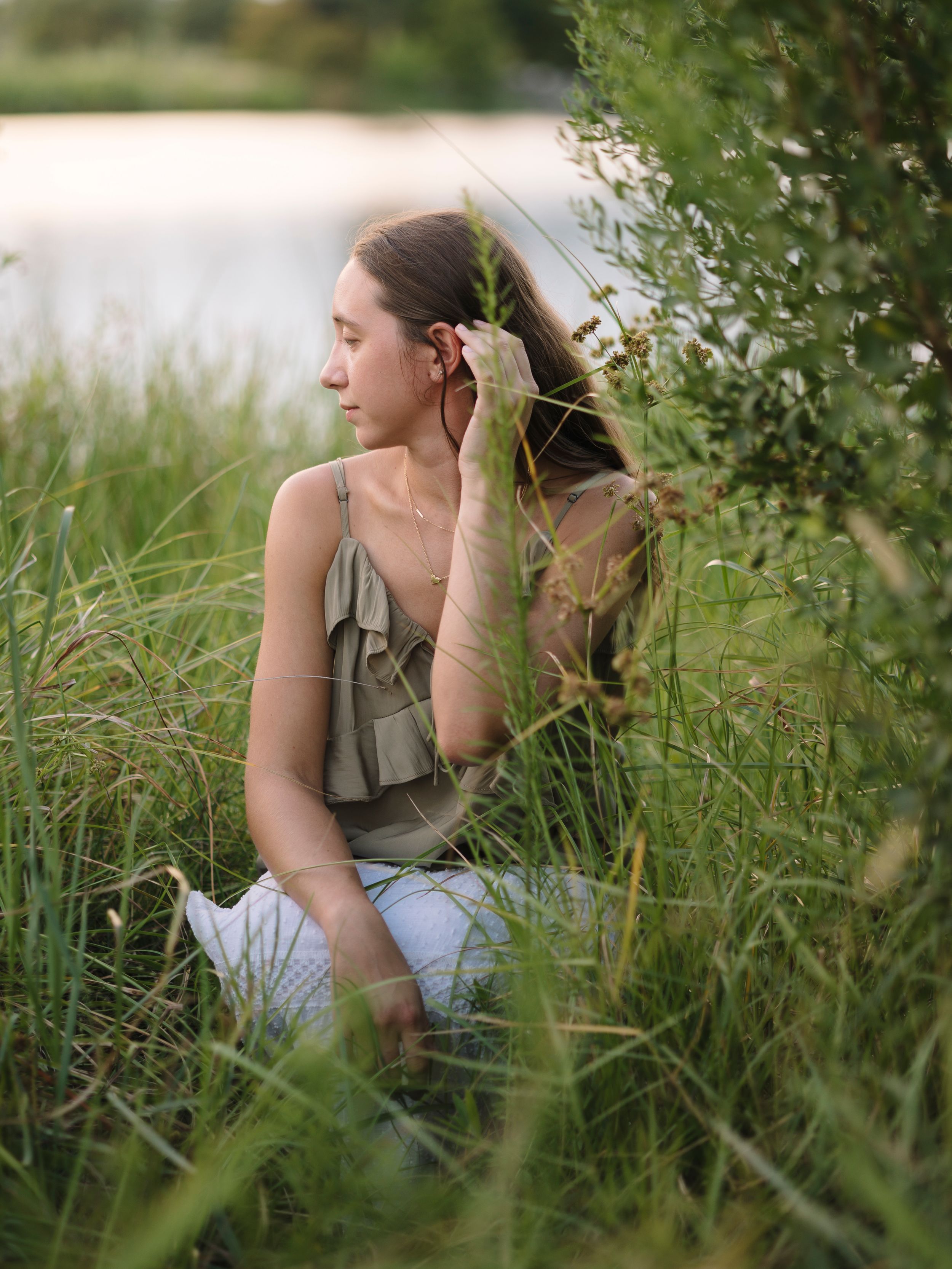 A person sits thoughtfully in tall summer grass wearing a casual tank top and jeans on a sunny day.
