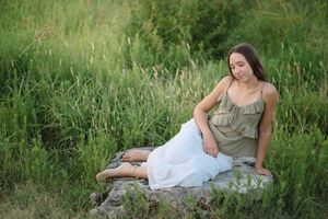 Someone rests gracefully among wildflowers and tall grass in a white dress during a golden hour photoshoot.