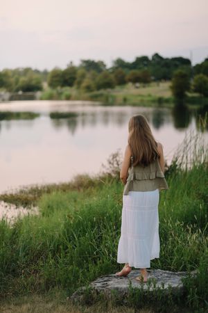 A white dress silhouetted against a tranquil lake while surrounded by tall grass and reeds at sunset.