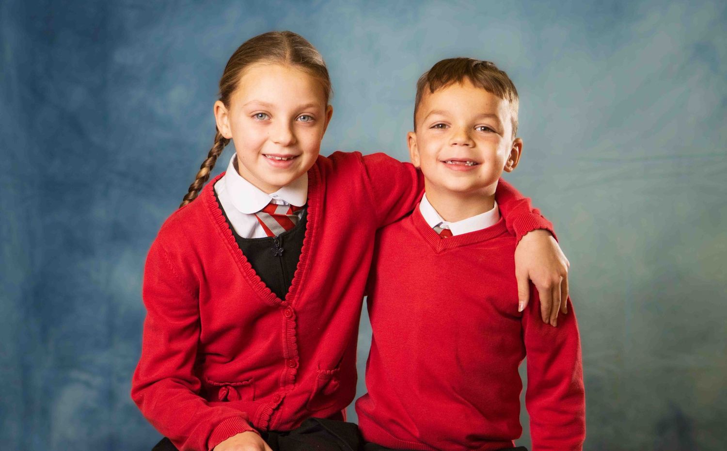 Two students in matching red school uniforms pose together against a blue studio backdrop.