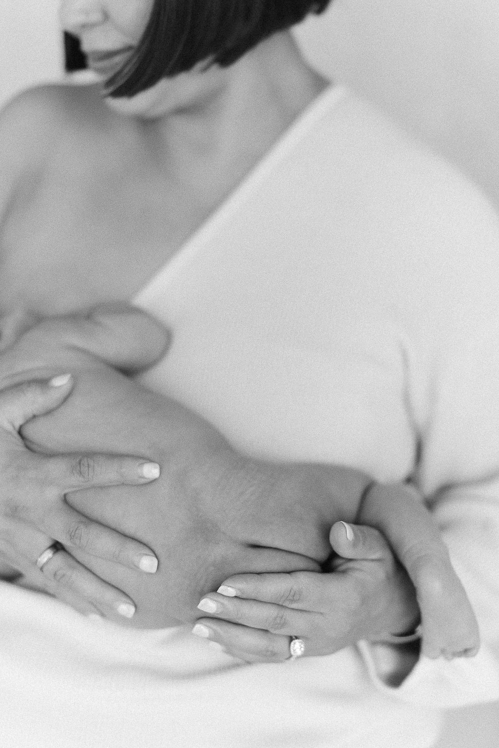 Black and white close up image of hands cradling a pregnant belly with a wedding ring visible on one finger.