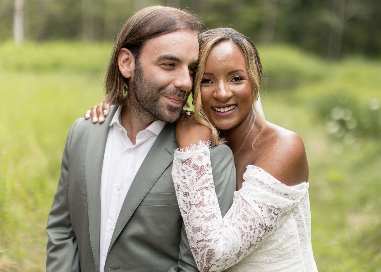 A couple embraces outdoors in wedding attire surrounded by lush greenery and natural lighting.