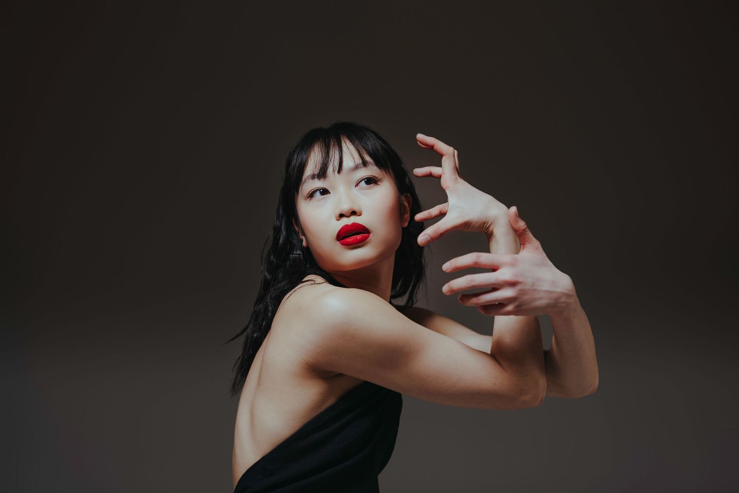 Model wearing bright red lipstick poses against dark background in dramatic black and white fashion photoshoot.