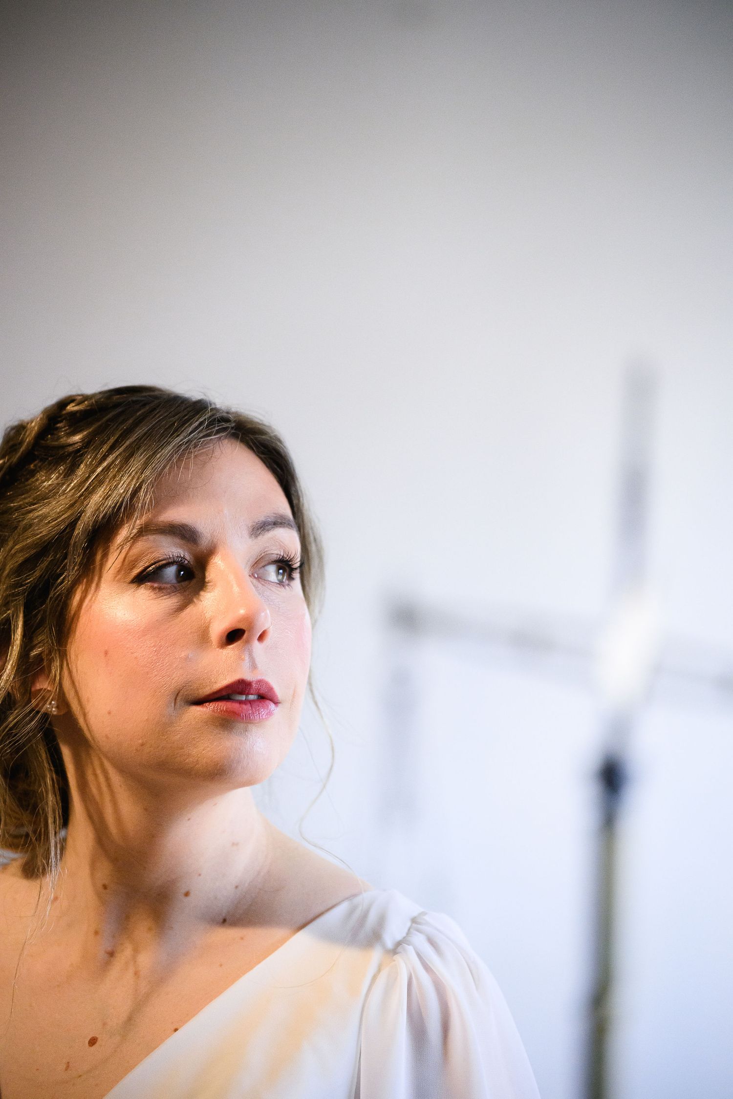 Close-up portrait of someone wearing a white dress with soft makeup and an updo hairstyle.