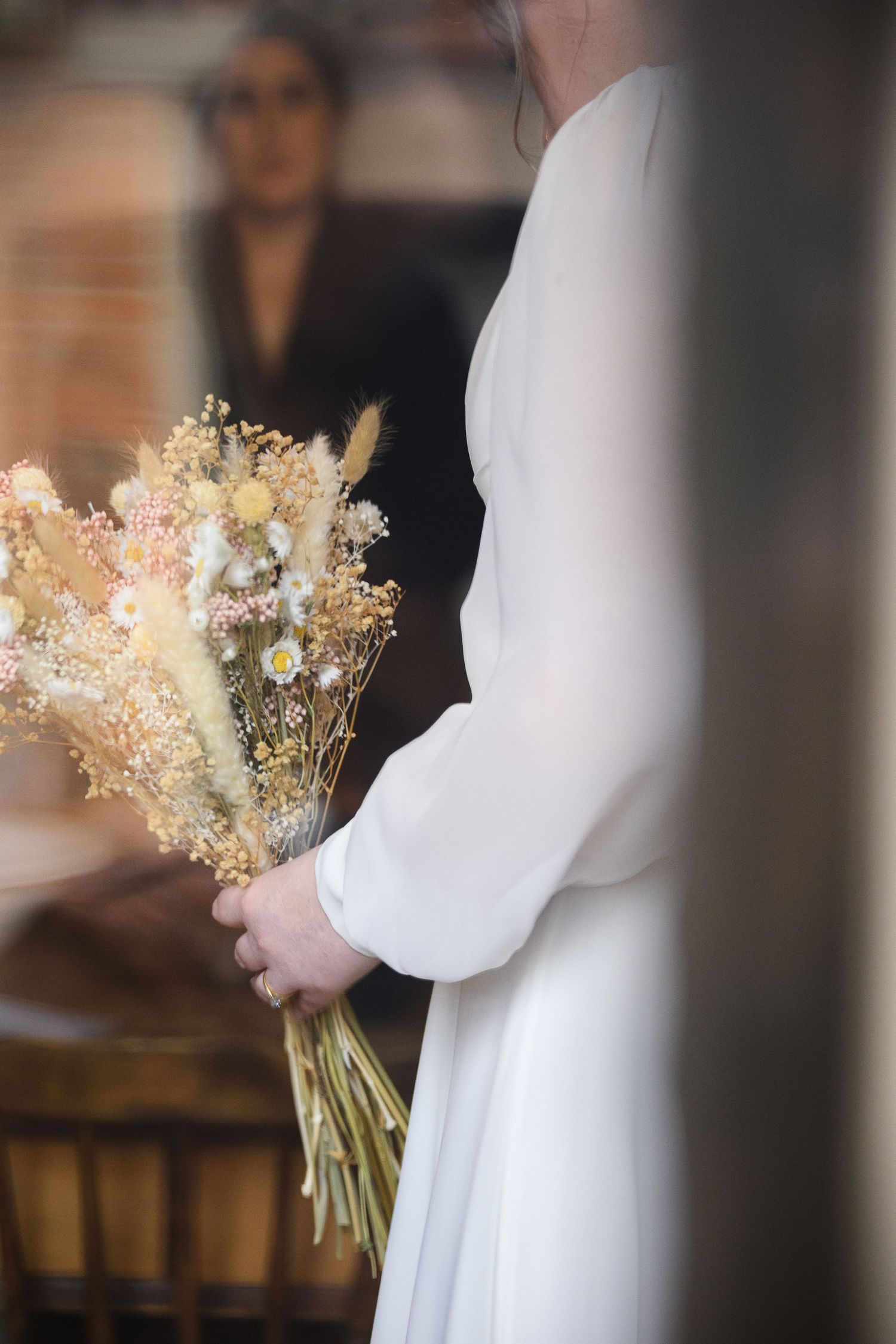 A bride in a simple white dress holds a delicate bouquet of baby's breath and dried flowers in a focused portrait.