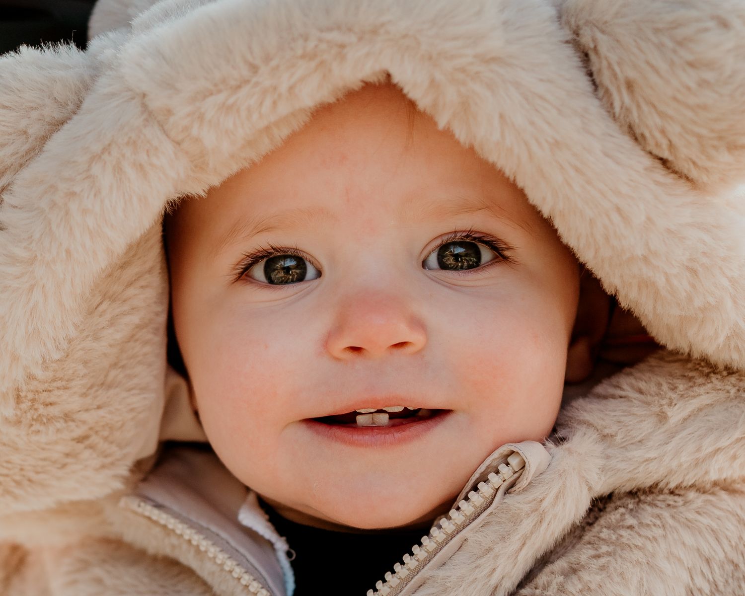 Close-up portrait shots showing playful expressions under cozy cream-colored blankets.