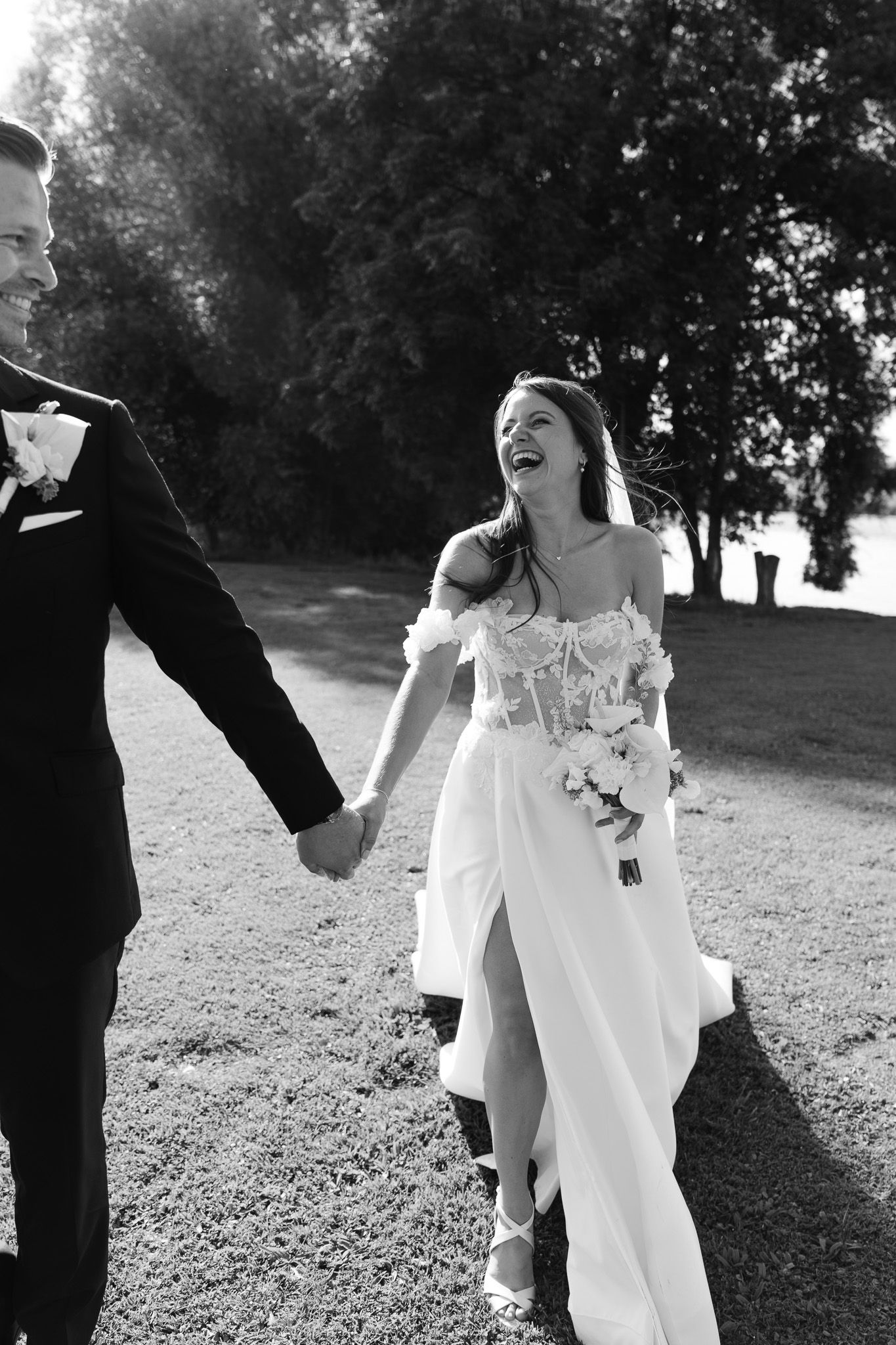 A joyful wedding couple holding hands and laughing while walking outdoors in black and white.